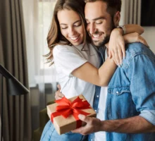 Beau jeune couple amoureux à la maison, célébrant la saint-valentin l'échange d'un paquet cadeau, s'embrassant.