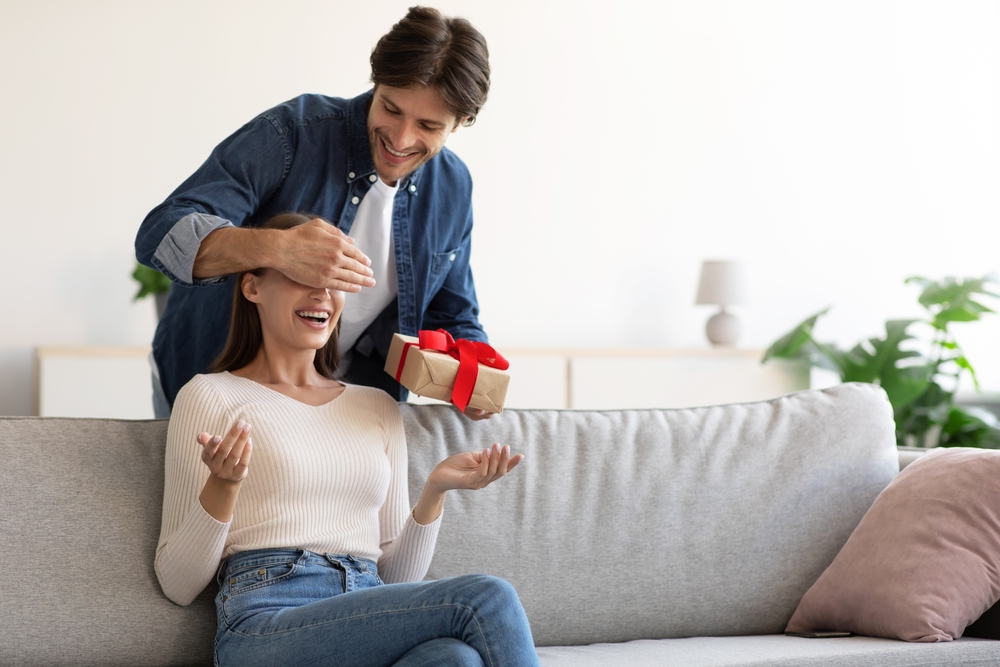 Un homme ferme les yeux à la femme, donne un cadeau dans une boîte pour surprendre l'épouse souriante. Il profite qu'elle soit assise tranquillement devant la télé pour lui offrir un cadeau de saint-valentin de dernière minute. 